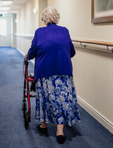 elderly woman pushing walker down hallway